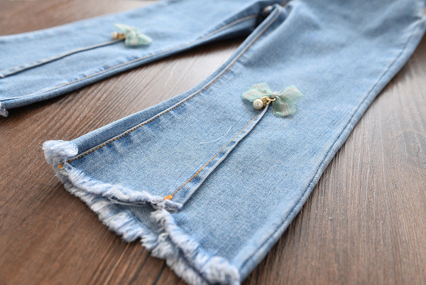 Mūsdienīgi bērnu džinsi meitenēm ar lentīti un saplēstiem motīviem